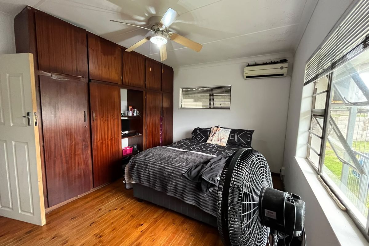 Bedroom featuring extensive built-in wooden cabinetry, polished wooden flooring, a ceiling fan, and a wall-mounted air conditioning unit.
