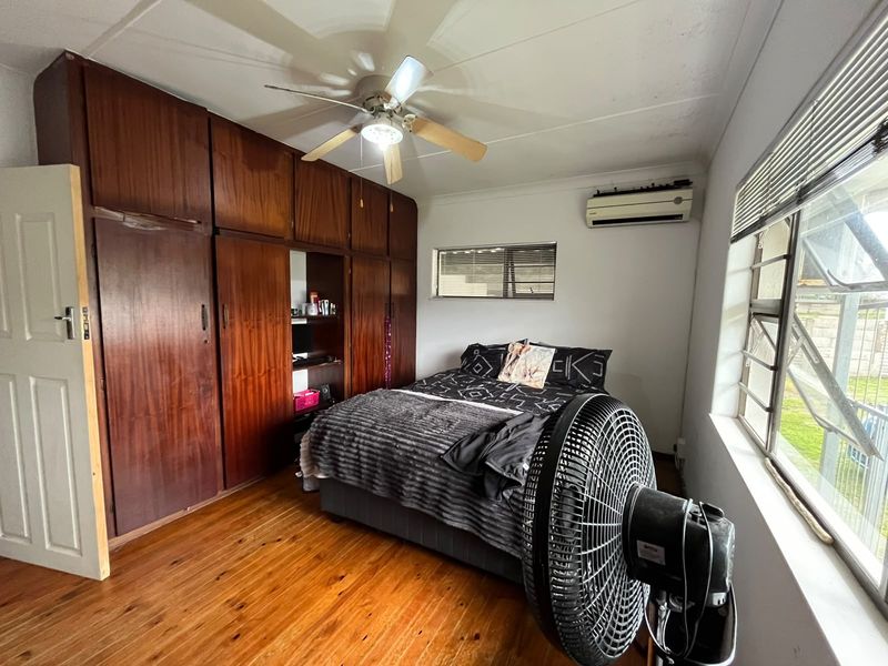 Bedroom featuring extensive built-in wooden cabinetry, polished wooden flooring, a ceiling fan, and a wall-mounted air conditioning unit.