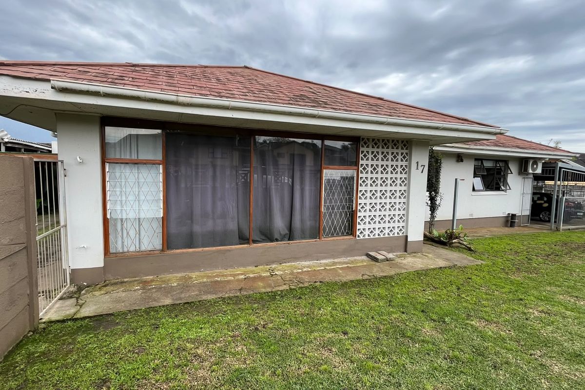 Rear view of the property featuring a tiled roof, concrete patio area, and decorative breeze block walling with security gates.