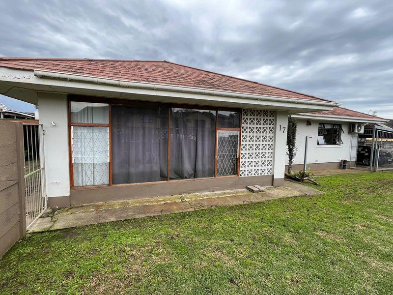 Rear view of the property featuring a tiled roof, concrete patio area, and decorative breeze block walling with security gates.
