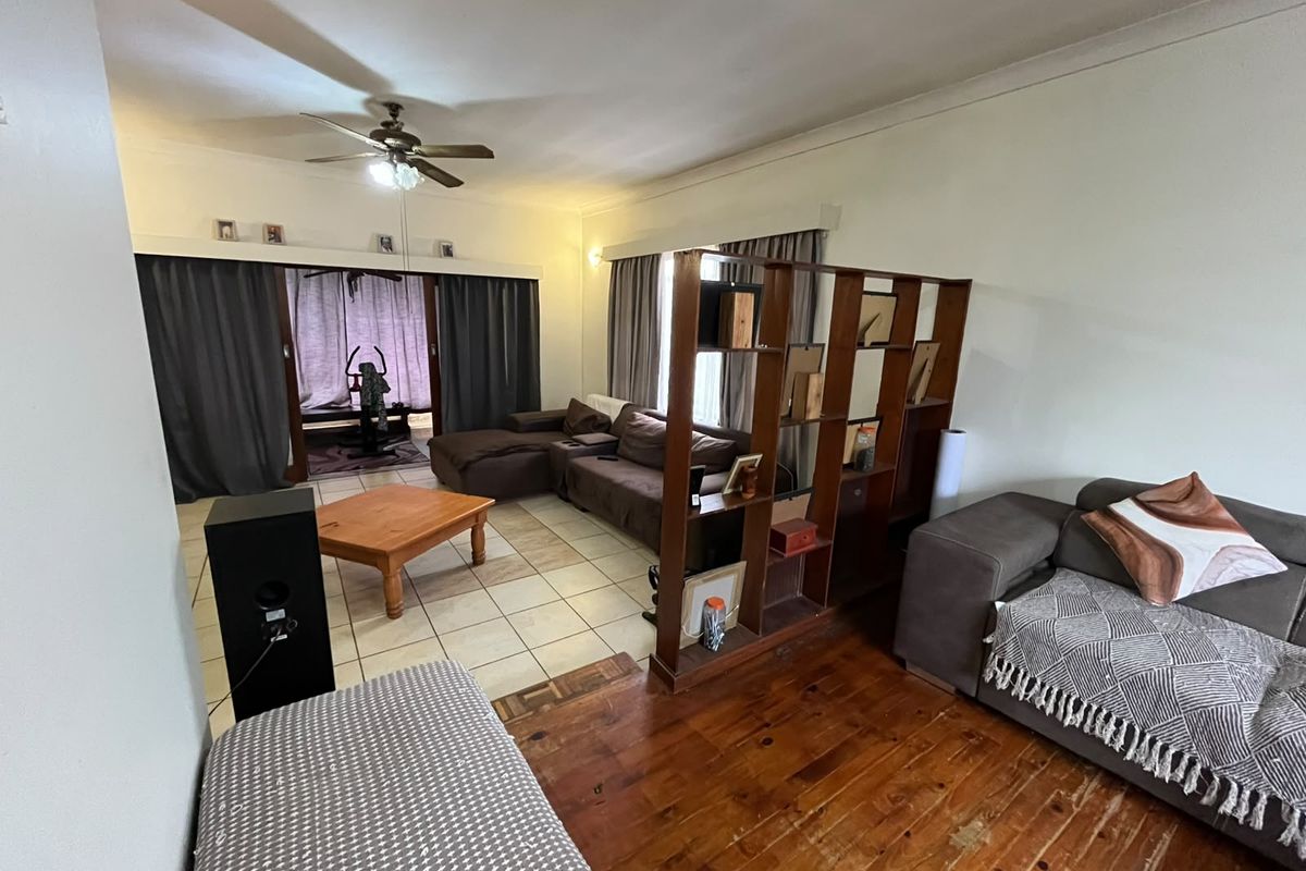 Spacious living area featuring a combination of tiled and wooden flooring, a ceiling fan, and sliding glass doors leading to an adjacent space.