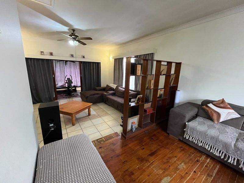 Spacious living area featuring a combination of tiled and wooden flooring, a ceiling fan, and sliding glass doors leading to an adjacent space.