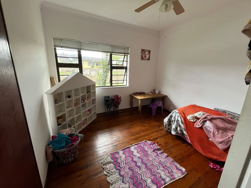 A bedroom featuring polished timber flooring, a ceiling fan, and aluminium-framed windows with venetian blinds.