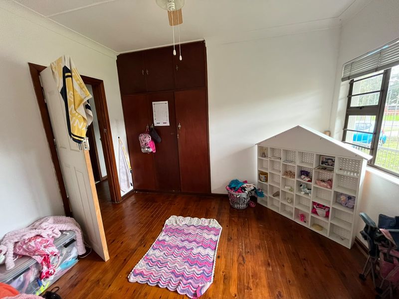 A bedroom featuring original wooden flooring, built-in wooden cupboards, and a ceiling fan, offering a functional space with potential for cosmetic updates.