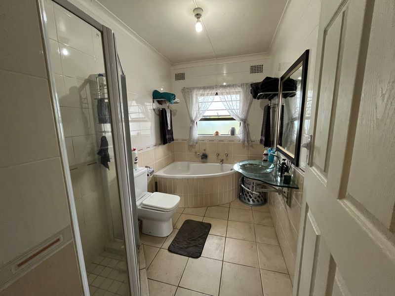 A functional bathroom featuring a corner bathtub, separate shower enclosure, and a modern glass vanity basin with tiled finishes throughout.