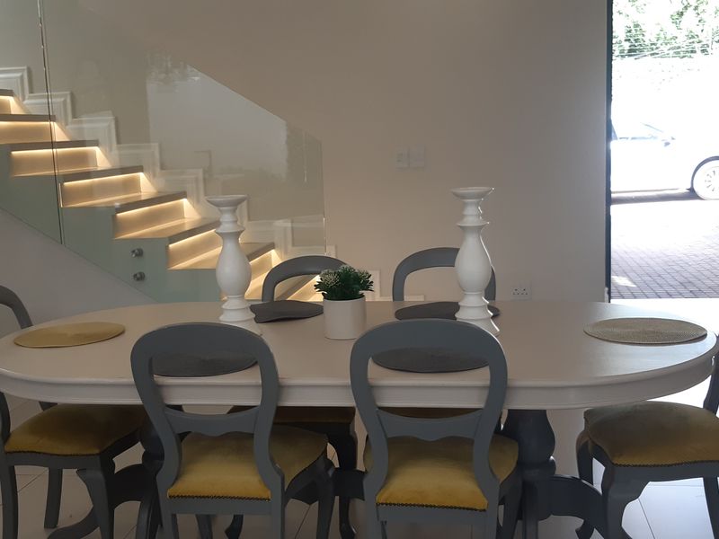 Modern dining area featuring a striking floating staircase with glass balustrade and integrated LED lighting, leading to an open-plan living space.