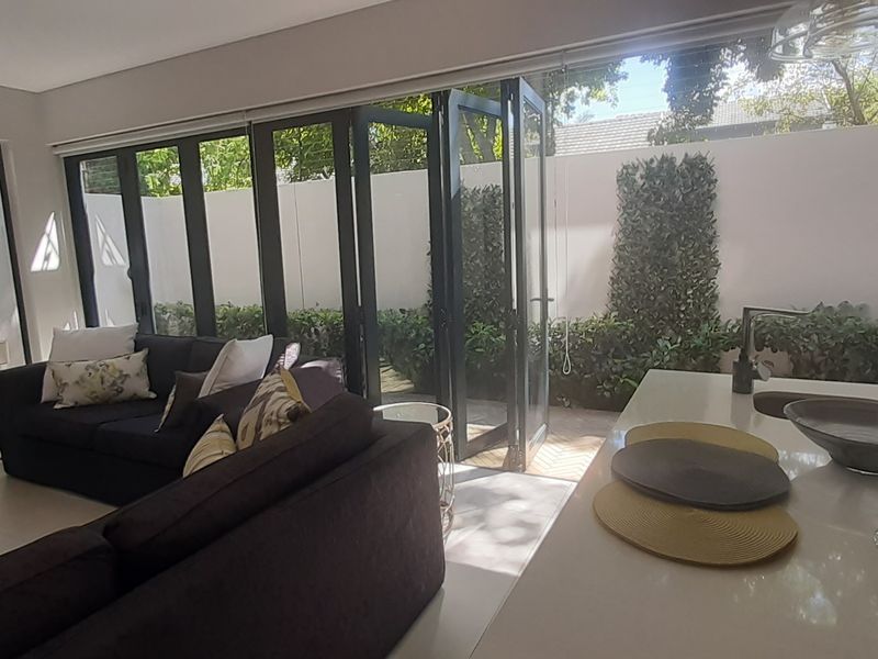Modern open-plan living area featuring a kitchen island with sink and large bi-fold doors opening to a private courtyard garden.