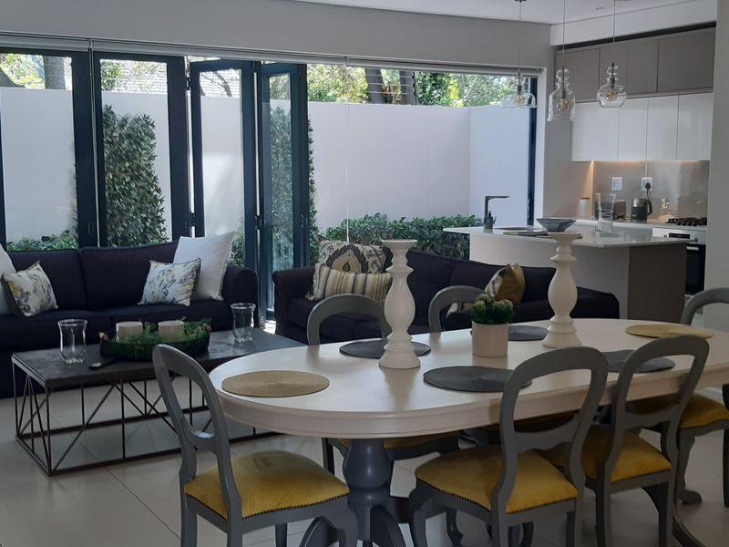 Modern open-plan living and dining area featuring sleek kitchen cabinetry, a central island, and large bi-fold doors opening to a private outdoor space.