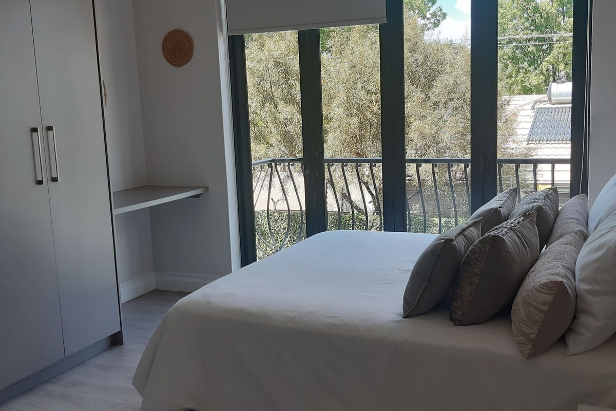 A well-lit bedroom featuring built-in cupboards, an integrated desk, and direct access to a private balcony through large glass doors.