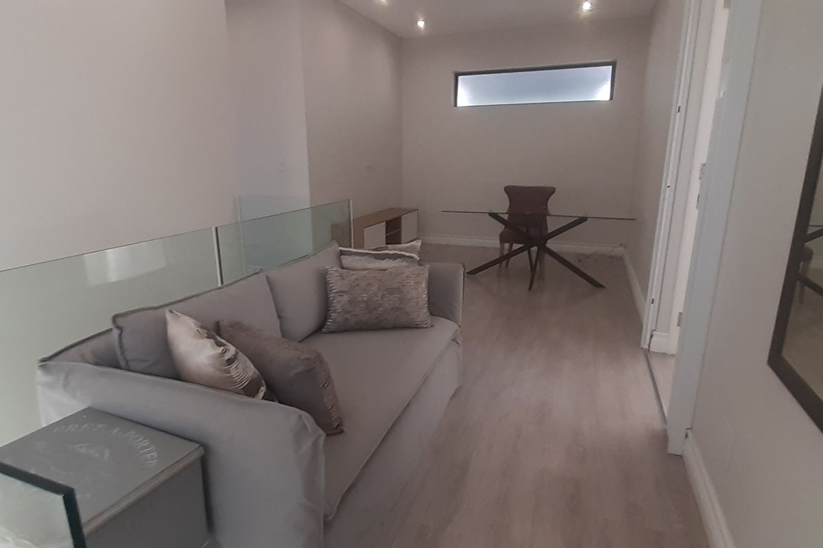 A bright living area featuring modern glass balustrades, recessed downlighting, and light-toned laminate flooring with a high-level clerestory window.