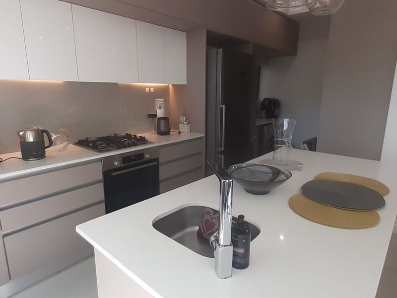 Modern kitchen featuring sleek handleless cabinetry, stone countertops, integrated gas hob, built-in oven, and a central island with an undermount sink.