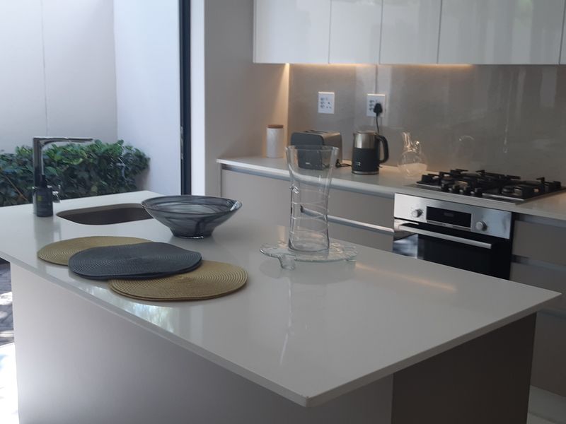 Modern kitchen featuring a central island with stone countertops, built-in oven, gas hob, and sleek cabinetry, with direct access to an outdoor patio area.