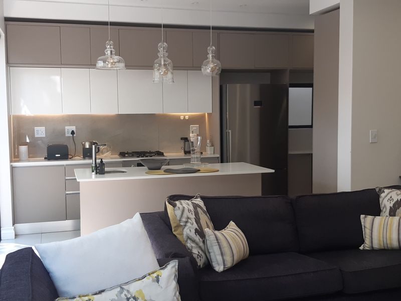 Modern open-plan living area featuring a sleek kitchen with island, high-end cabinetry, and seamless flow to the outdoor patio through large sliding glass doors.
