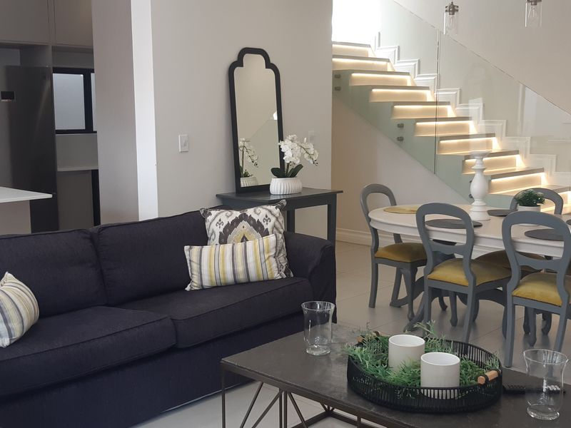 Modern open-plan living and dining area featuring a sleek kitchen, contemporary staircase with integrated lighting, and high-quality tiled flooring throughout.
