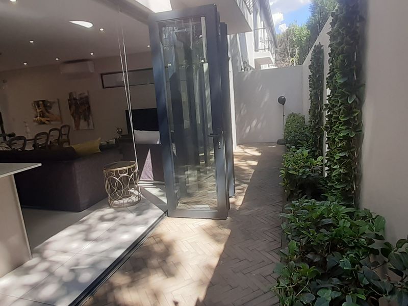 Open-plan living area seamlessly connecting to a private paved patio through modern bi-fold doors, featuring a vertical garden and contemporary finishes.