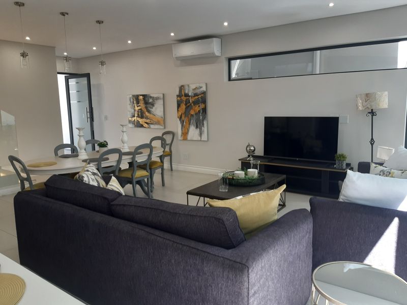 A bright and modern open-plan living and dining area featuring tiled floors, recessed lighting, and a wall-mounted air conditioning unit.