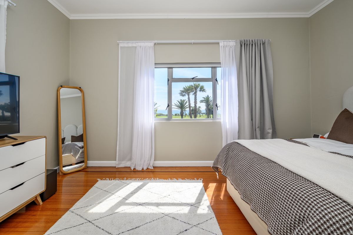 A well-maintained bedroom featuring polished hardwood flooring, neutral wall tones, and a window offering pleasant outdoor views.