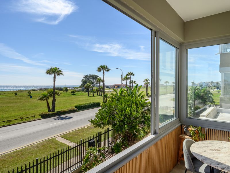 Enclosed balcony featuring modern aluminium sliding windows, slatted timber wall cladding, and expansive views over the coastal landscape.