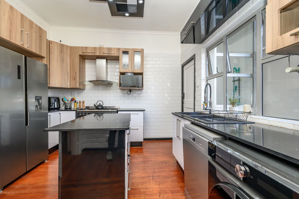 Modern kitchen featuring wood-tone and black cabinetry, a central island, subway tile backsplash, and high-quality integrated appliances with warm hardwood flooring.