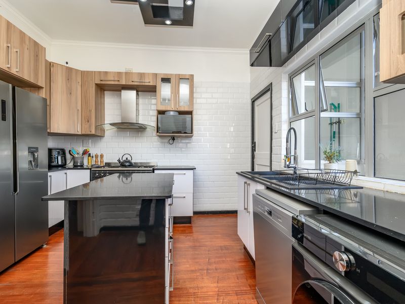 Modern kitchen featuring wood-tone and black cabinetry, a central island, subway tile backsplash, and high-quality integrated appliances with warm hardwood flooring.