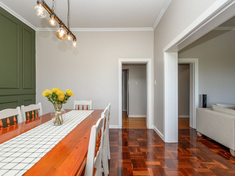 A well-maintained dining area featuring rich parquet flooring, elegant crown molding, and a striking green accent wall with decorative paneling.
