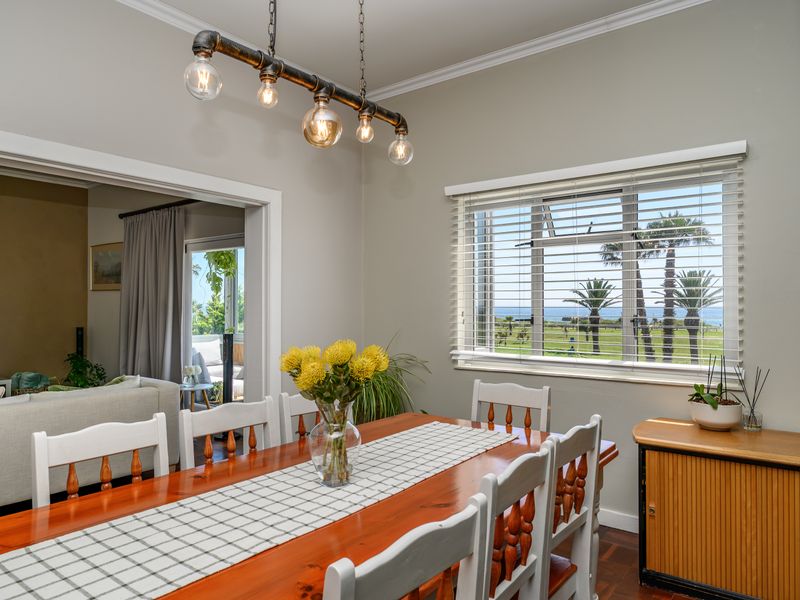 A bright dining room featuring parquet flooring, an industrial-style pendant light, and a window offering scenic views of the surrounding landscape and ocean.