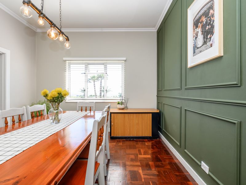 A well-maintained dining room featuring classic parquet flooring, decorative wainscoting on the feature wall, and natural light through venetian blinds.