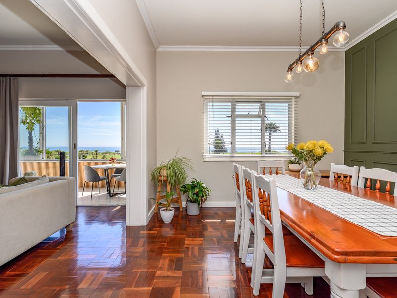 Bright open-plan dining area featuring rich parquet flooring, decorative wall paneling, and seamless access to a balcony with scenic coastal views.