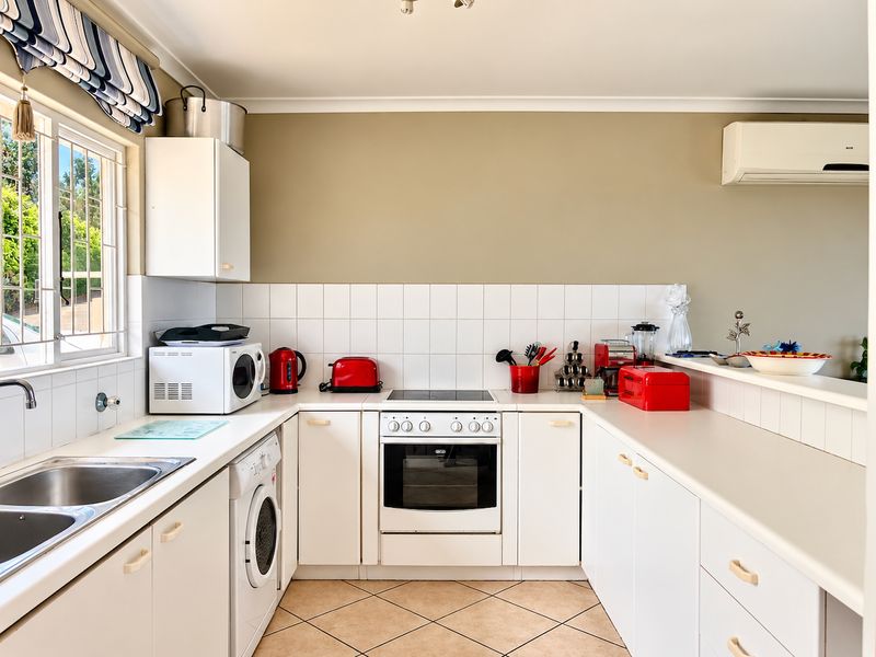 A functional kitchen featuring white cabinetry, laminate countertops, tiled backsplash, and integrated electric cooking appliances, complemented by tiled flooring and an air conditioning unit.