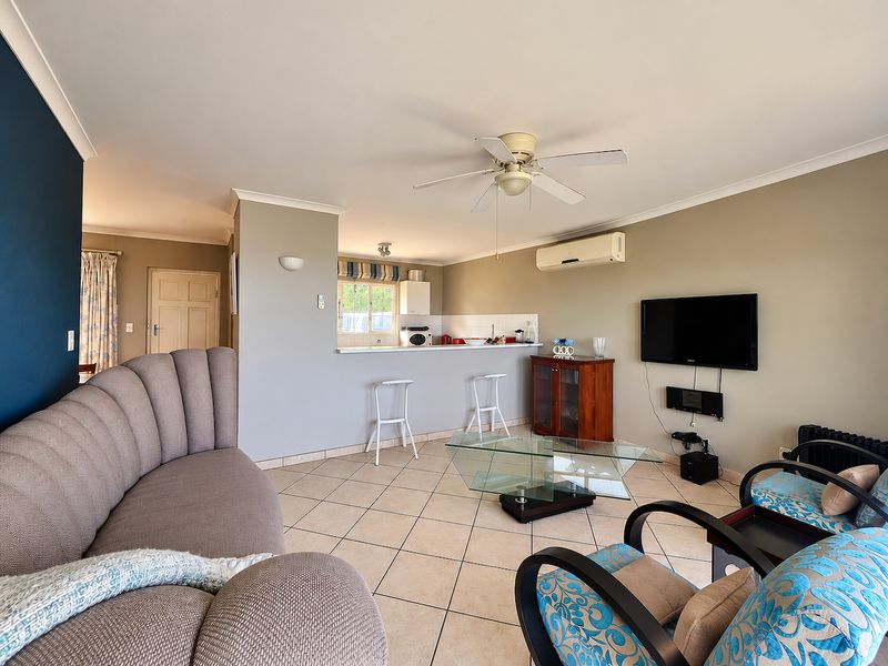 Open-plan living area featuring tiled floors, a breakfast bar connecting to the kitchen, ceiling fan, and wall-mounted air conditioning unit.