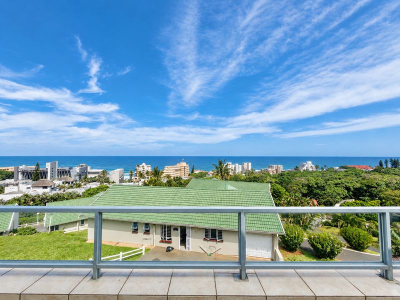 Elevated balcony view overlooking the surrounding coastal neighborhood, lush greenery, and the ocean horizon.