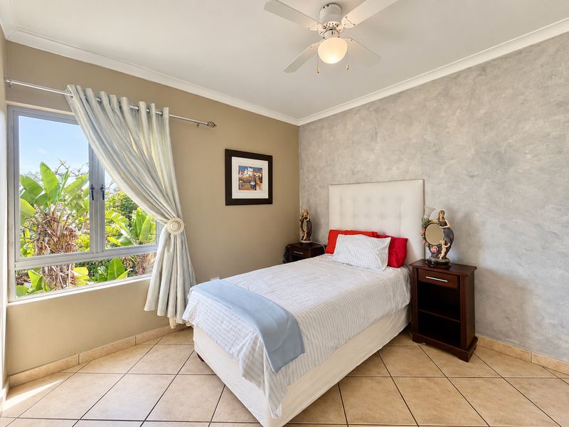A well-maintained bedroom featuring tiled flooring, a ceiling fan, and a textured feature wall with natural light from the window.