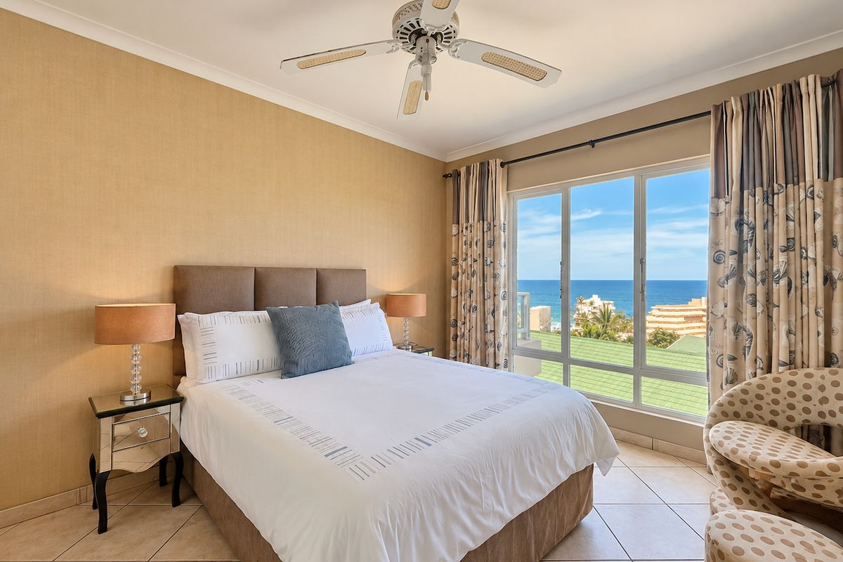 A well-maintained bedroom featuring tiled flooring, a ceiling fan, and a large window offering expansive ocean views.