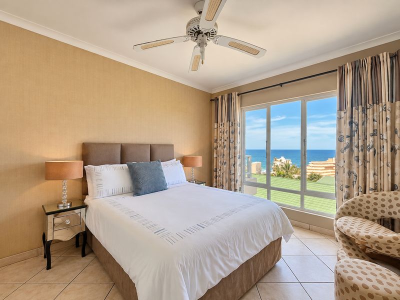 A well-maintained bedroom featuring tiled flooring, a ceiling fan, and a large window offering expansive ocean views.