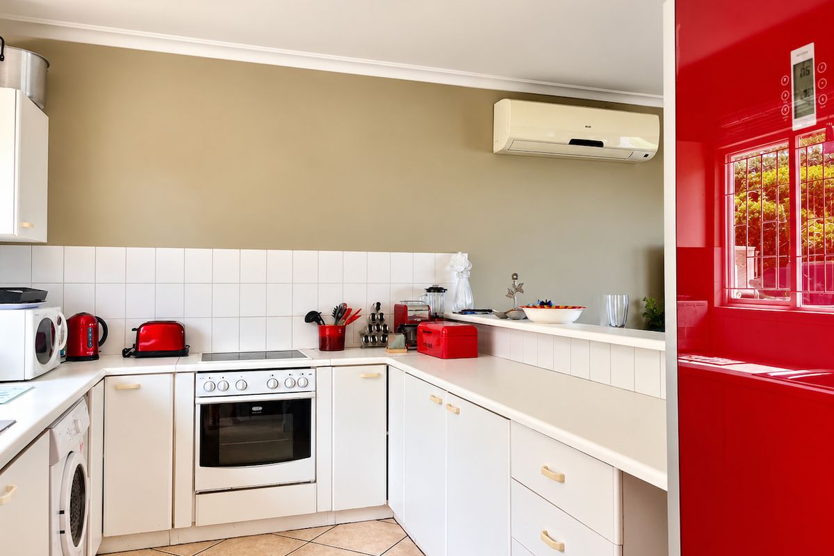 A functional kitchen featuring white cabinetry, tiled splashbacks, a built-in oven with electric hob, and a wall-mounted air conditioning unit.