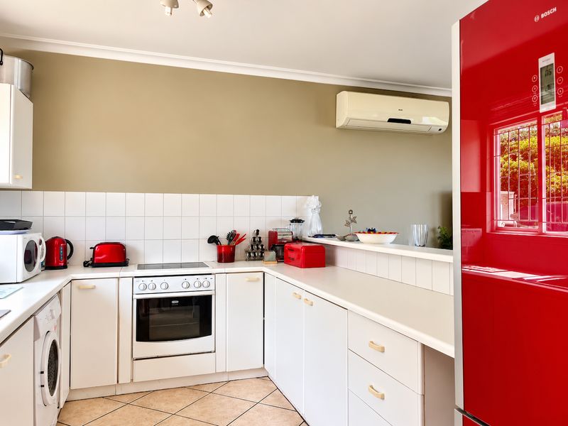A functional kitchen featuring white cabinetry, tiled splashbacks, a built-in oven with electric hob, and a wall-mounted air conditioning unit.
