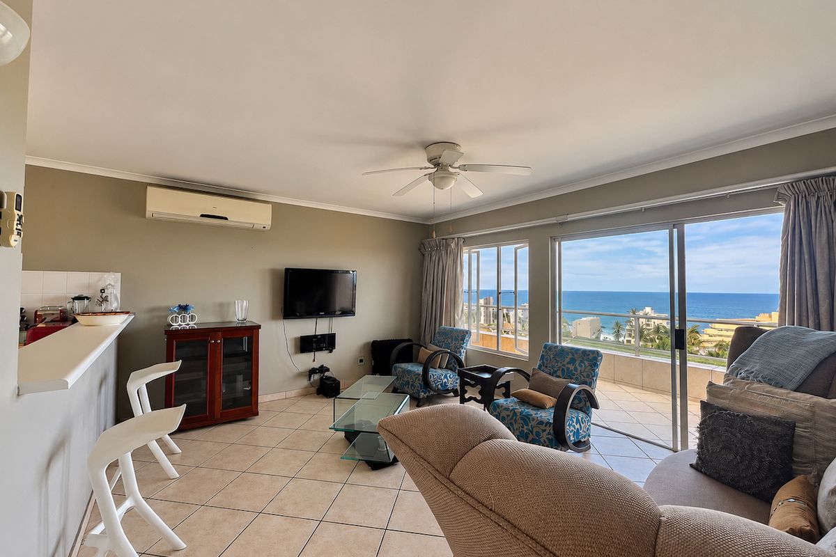 Open-plan living area featuring tiled floors, a ceiling fan, air conditioning, and large sliding doors opening to a balcony with ocean views.