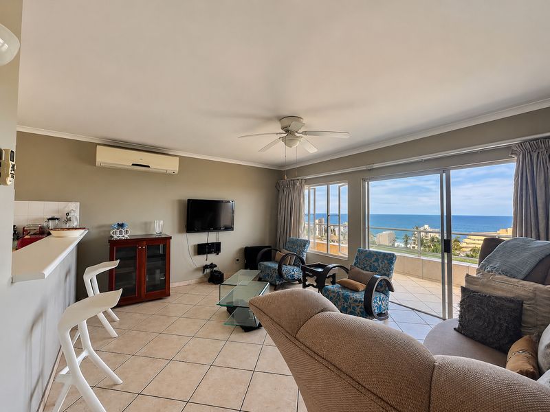 Open-plan living area featuring tiled floors, a ceiling fan, air conditioning, and large sliding doors opening to a balcony with ocean views.