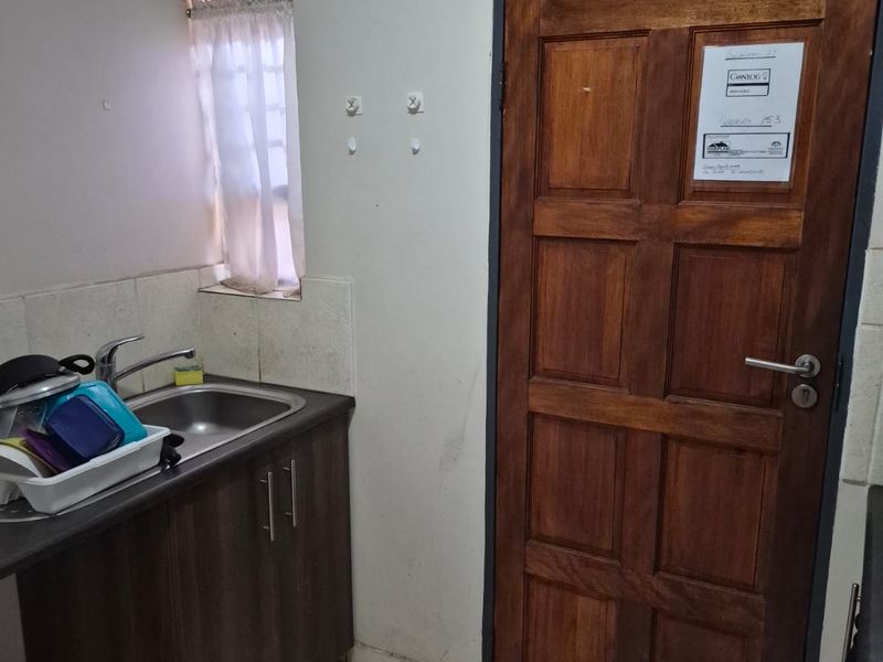 A functional scullery area featuring a stainless steel sink, built-in base cabinetry, tiled flooring, and a solid wood door.