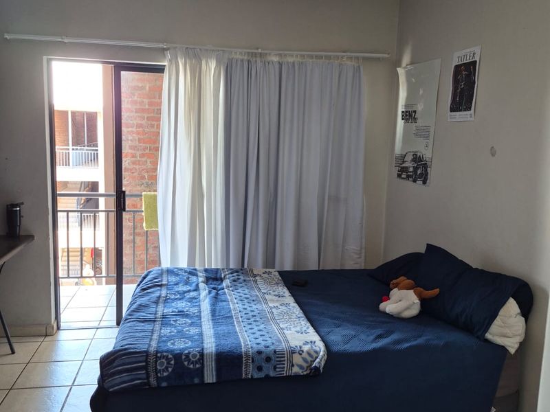 A bedroom featuring tiled flooring and a sliding glass door providing access to a balcony, offering natural light and outdoor connectivity.