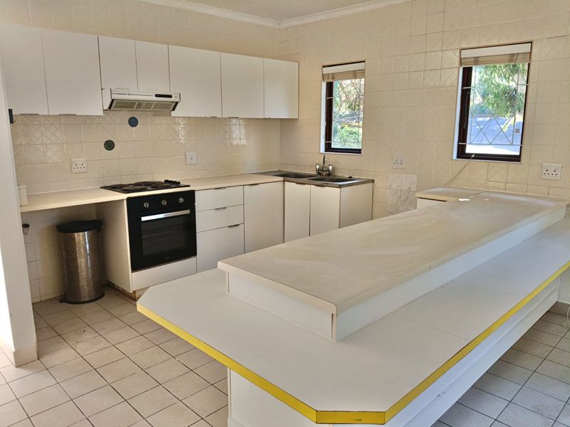 A functional kitchen featuring white cabinetry, built-in oven with gas hob, double sink, and a spacious breakfast bar with tiled flooring throughout.