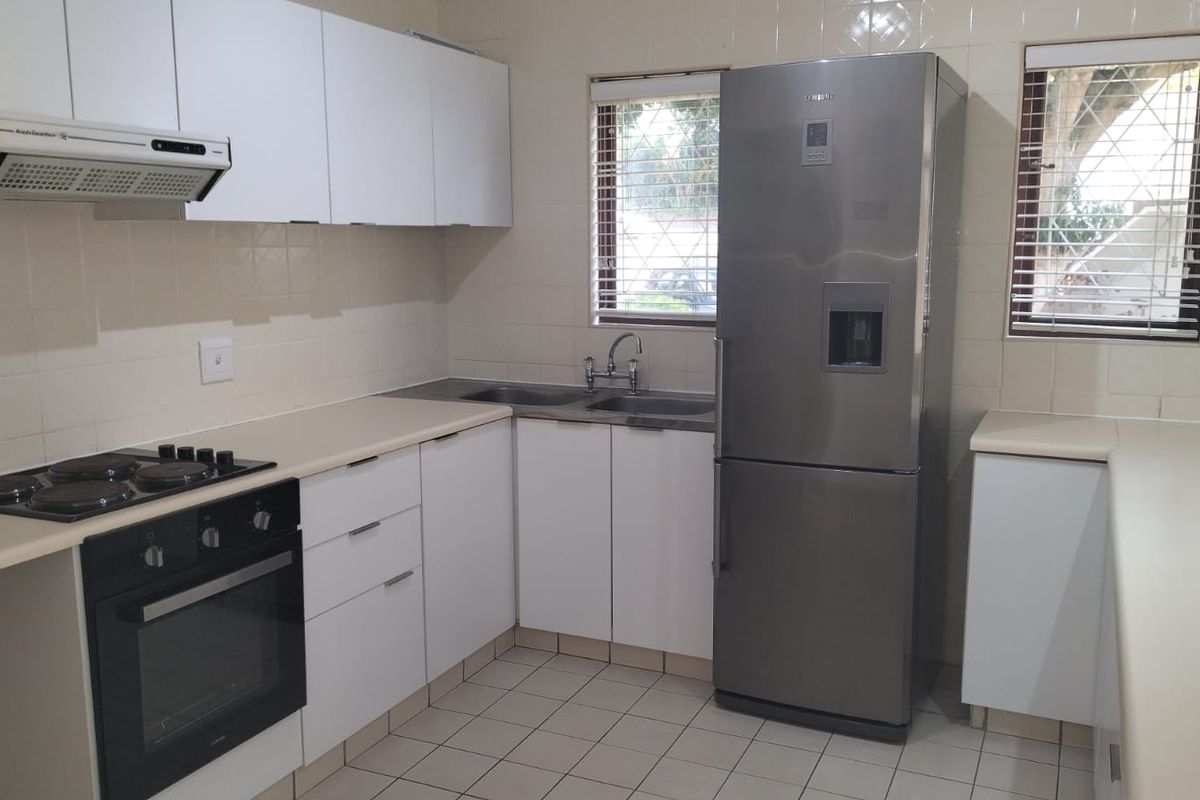 A functional kitchen featuring white cabinetry, laminate countertops, tiled splashbacks, and integrated appliances including an oven, hob, and extractor fan.