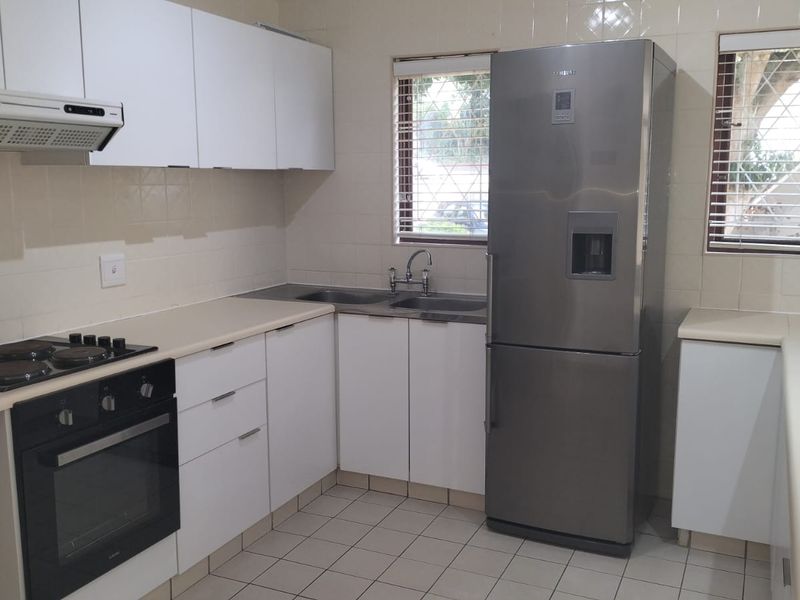 A functional kitchen featuring white cabinetry, laminate countertops, tiled splashbacks, and integrated appliances including an oven, hob, and extractor fan.