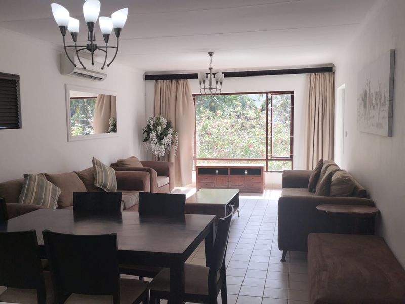 Spacious open-plan living and dining area featuring tiled flooring, large windows with natural light, and a wall-mounted air conditioning unit.