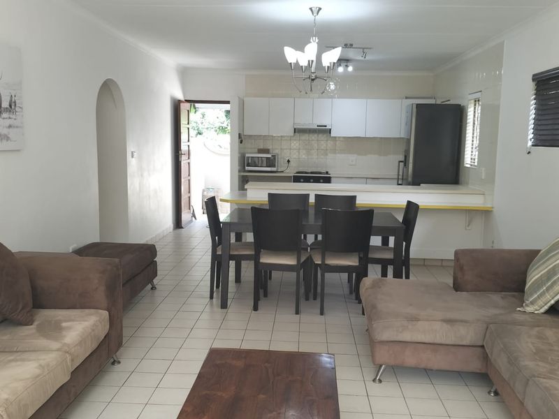 Open-plan living and dining area featuring a functional kitchen with built-in cabinetry, breakfast counter, and tiled flooring throughout.
