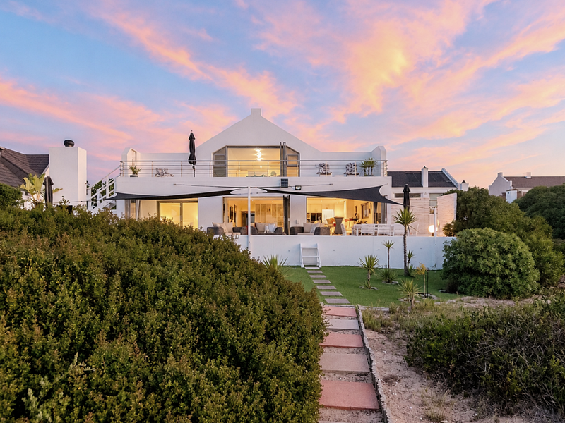 A beautiful rear view of the property at sunset, featuring a spacious patio, upper balcony, and a well-maintained garden with a stone pathway.