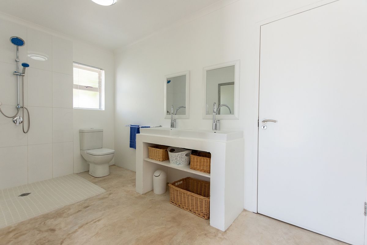 A bright and modern bathroom featuring a double vanity, walk-in shower with tiled enclosure, and polished concrete flooring.