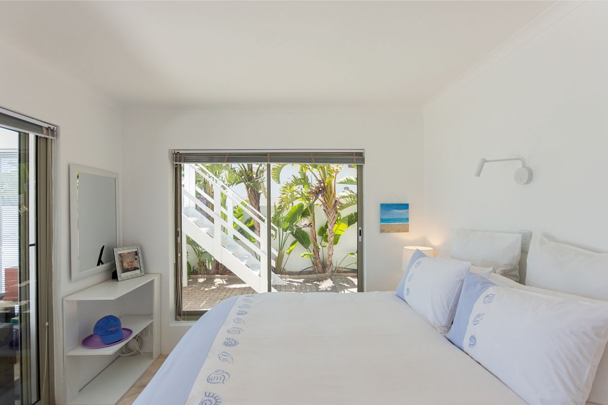 A bright bedroom featuring sliding glass doors that open to an outdoor patio area with stairs and lush greenery.