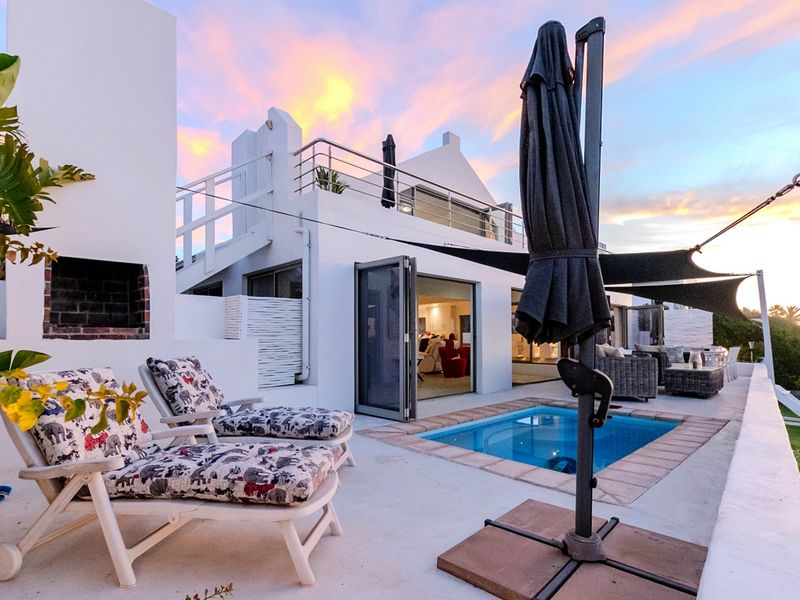 Outdoor pool area featuring a built-in fireplace, paved patio, and access to the main residence via bi-fold doors, set against a sunset backdrop.