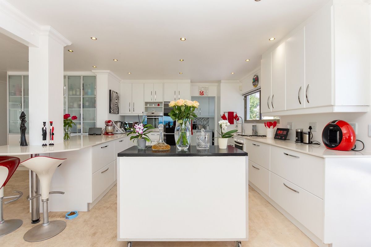 Modern kitchen featuring white cabinetry, stone countertops, a central island, and integrated appliances with recessed lighting throughout.